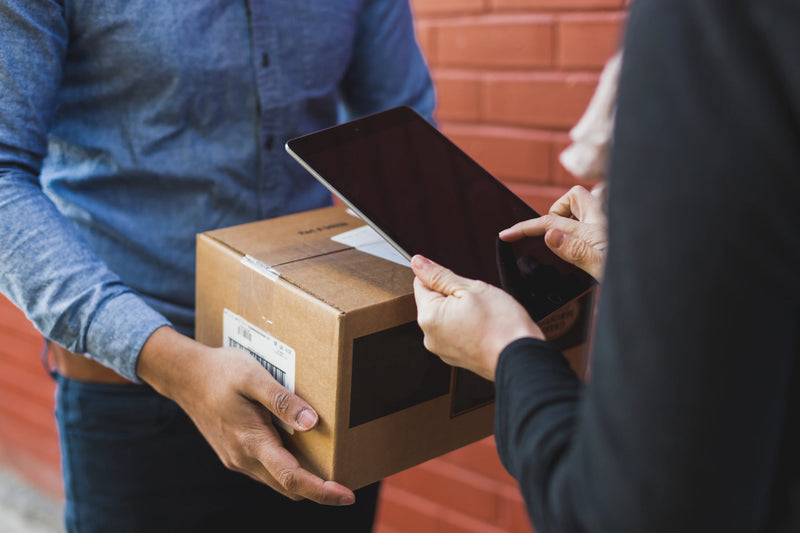 Person receiving a package and using a tablet for verification against a brick wall background